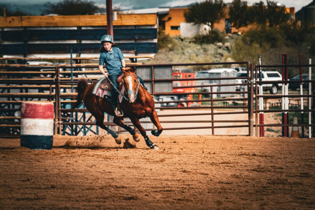 young girl riding horse around a barrel